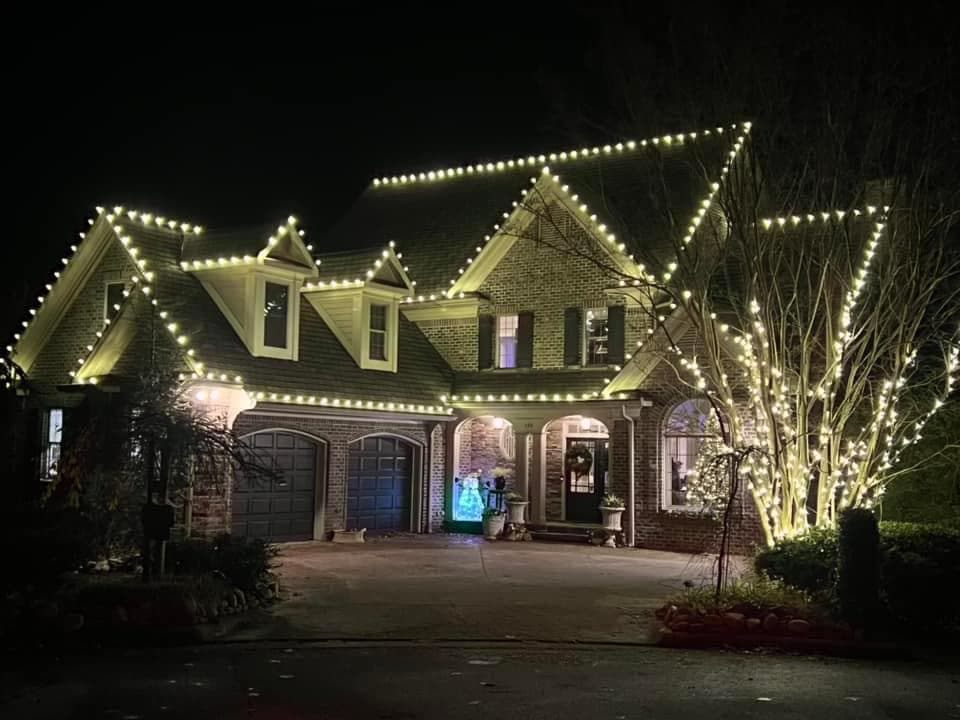 Brick home with peaked roofline lights and fully wrapped tree